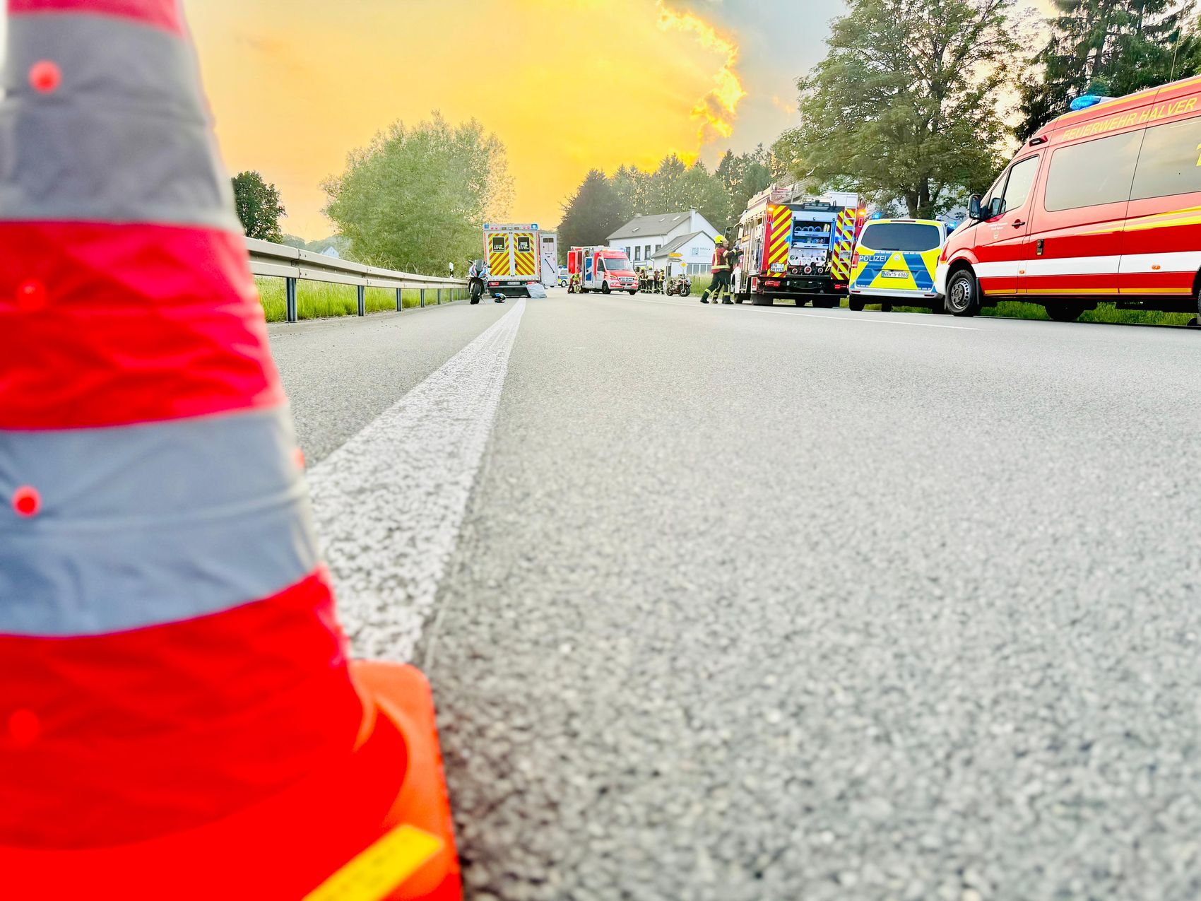 Mehrere Einsatzfahrzeuge stehen auf einer gesperrten Straße, im Vordergrund ein roter Verkehrskegel.